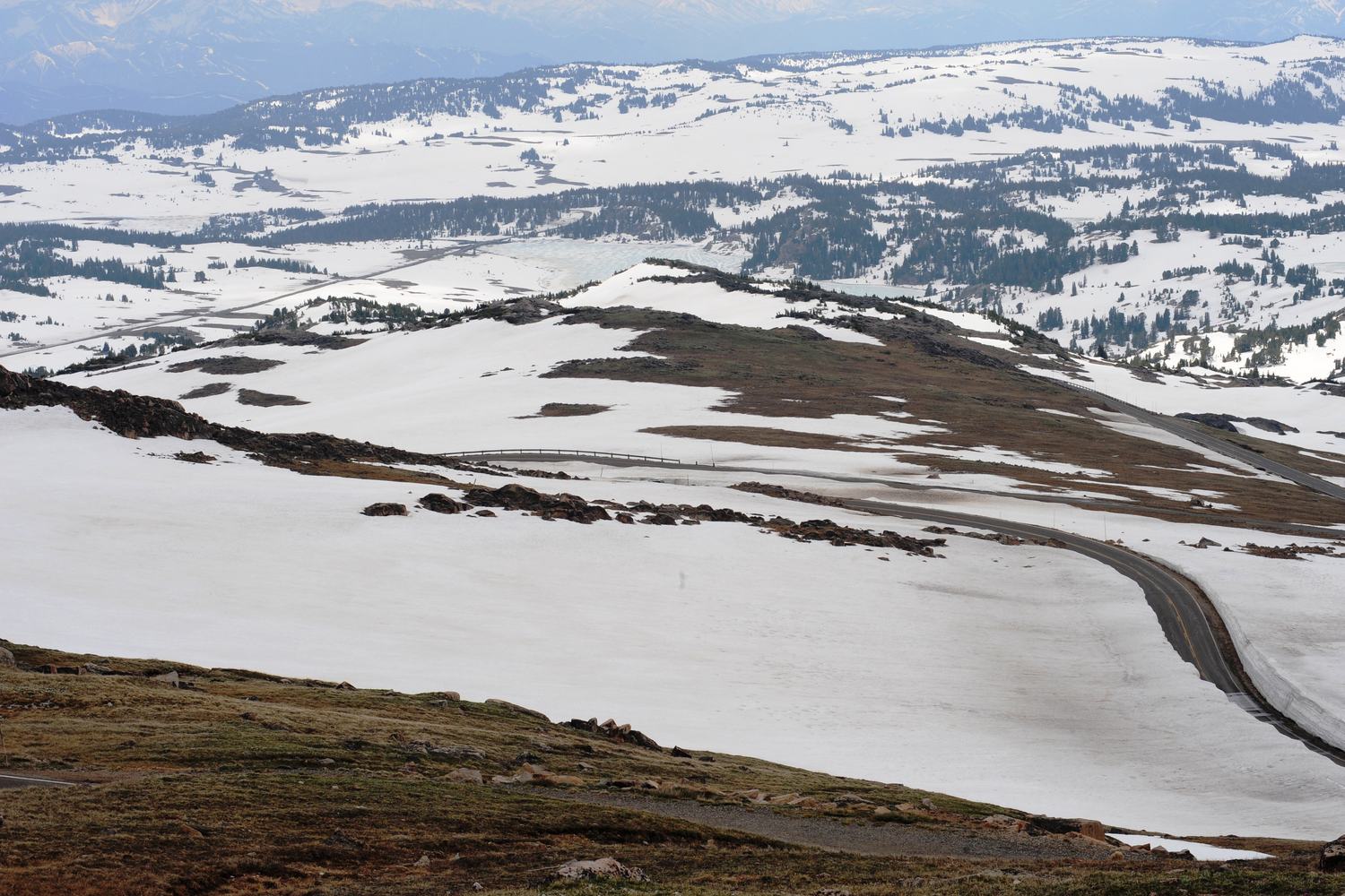The road over the west summit of Beartooth Pass winding between snowfields and bare tundra.